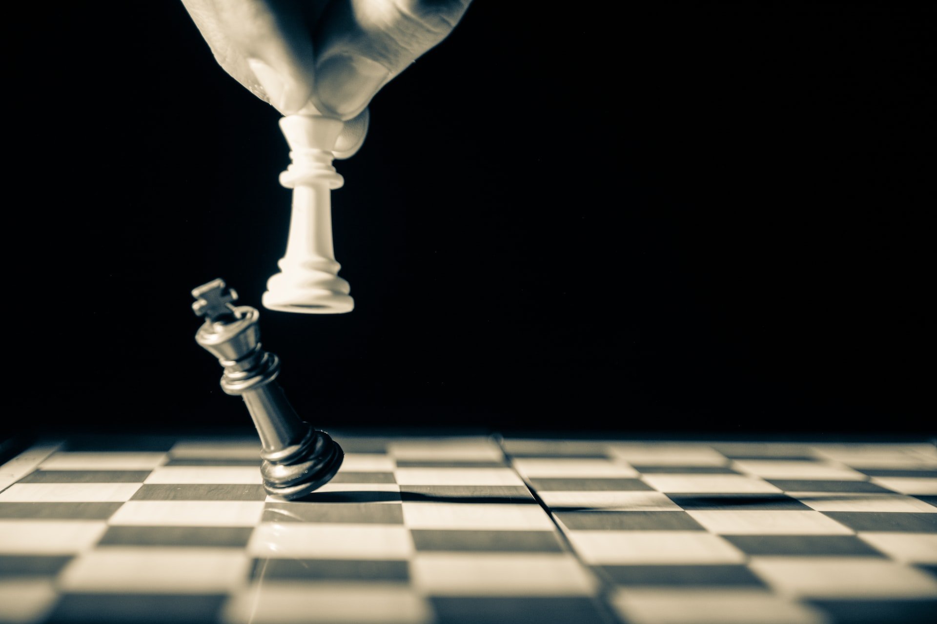 Close up of white king taking down black king. Hand and fingers and chess board with vintage look.